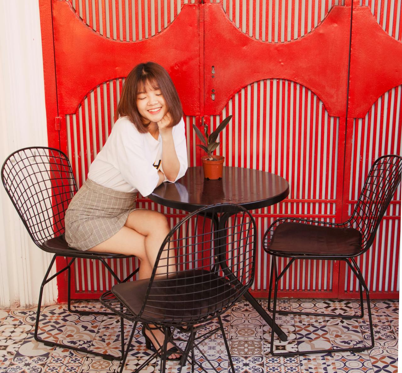 Smiling young woman sitting at a table in an outdoor café with vibrant decor.
