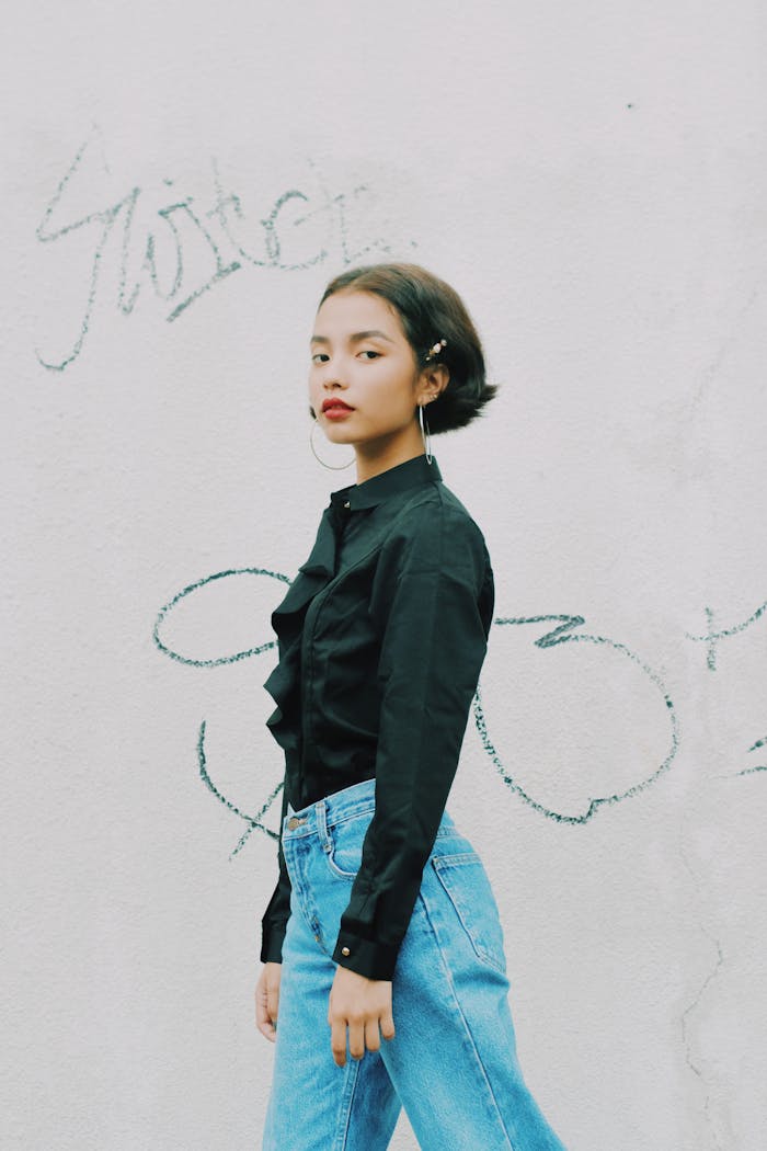 A young woman in casual attire poses confidently against a graffiti wall.